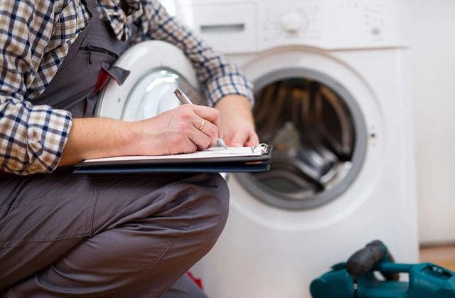 A person is writing on paper in front of a washing machine.